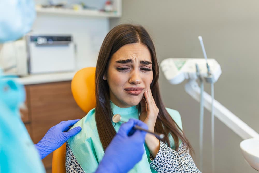 Young woman holding cheek in chair at dentist having toothache shot.